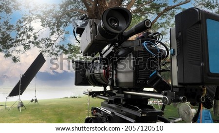 Movie Camera. Behind the video camera that for recording film commercial or movie at outdoor location. 35 mm film styled 4K digital camera and tripod dolly crane for video production. film industry. Royalty-Free Stock Photo #2057120510