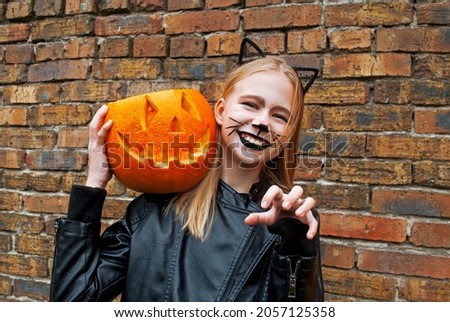 Beautiful teenager girl dressed as a black cat for Halloween. Child holding a pumpkin monster for Halloween. 
