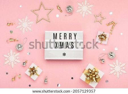 Merry Xmas text on white Lightbox with gift boxes, holiday silver and gold decorations, snowflakes on pink paper background. Flat lay, top view, copy space. Festive Christmas  winter time.