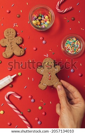 Christmas gingerbread cookie preparation process with gingerbread man, icing, sugar sprinkles and candy canes on a red table background. New year wallpaper flat lay.
