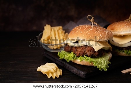 A set of homemade delicious burgers of beef, onion, cheese and lettuce on a dark wooden background. Fat unhealthy food close-up. With copy space.