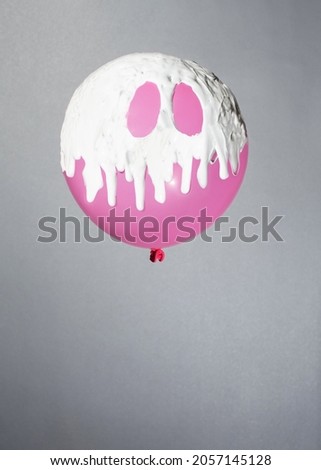 pink balloon with white paint on grey background. minimal concept. halloween aesthetic