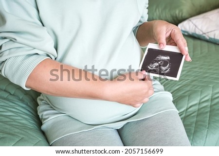 Pregnant belly with ultrasound result picture. Woman see unborned kid face. Waiting baby. Expecting child health therapy. Gynecologist check Royalty-Free Stock Photo #2057156699