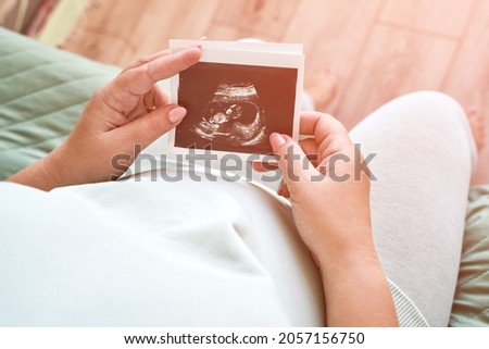 Pregnant belly with ultrasound result picture. Woman see unborned kid face. Waiting baby. Expecting child health therapy. Gynecologist check Royalty-Free Stock Photo #2057156750