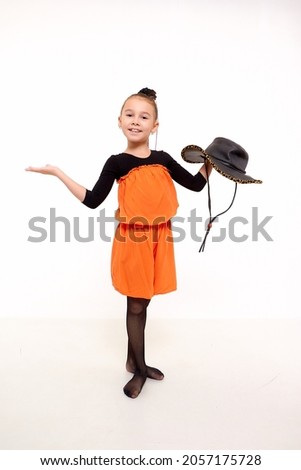 Funny girl in orange dress with hat in the studio with white background during photo shoot. Cute young ballerina inside of the room