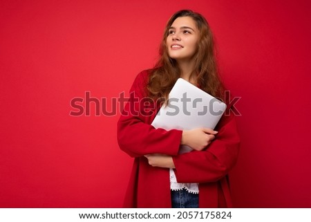 Photo of mysterious pretty young dark hair curly female student holding close netbook wearing red cardigan and white blouse looking to the side isolated over red background