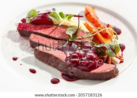 Venison steak with baked vegetables isolated on white plate. Meat steak medium rare roasted with carrot, beetroot and mashed potatoes with cherry sauce. Wild meat in restaurant menu Royalty-Free Stock Photo #2057183126