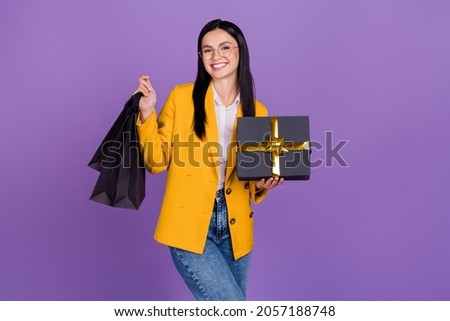 Photo of attractive beautiful young lady wear yellow jacket spectacles smiling holding gift packages isolated violet color background