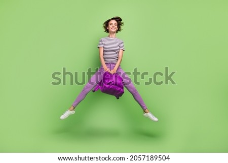 Photo of beautiful sweet young lady wear striped t-shirt rucksack jumping high smiling isolated green color background
