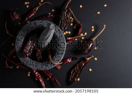 Stone molcajete with dried peppers around it. Molcajete is used to grind vegetables and prepare Mexican sauces. Royalty-Free Stock Photo #2057198105