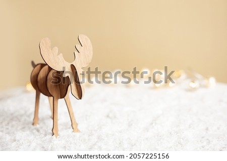 Christmas deer. Decorative wooden reindeer toy on pastel beige background. Happy new year 2022. Winter Greeting card with snow and light. Handmade figure deer . Eco style diy. Copy space.