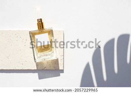 Transparent bottle of perfume with white label on stone plate on a white background. Fragrance presentation with daylight. Trending concept in natural materials with palm leaf shadows. Royalty-Free Stock Photo #2057229965