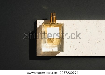 Transparent bottle of perfume with white label on stone plate on a grey background. Fragrance presentation with daylight. Trending concept in natural materials . Women's and men's essence. Royalty-Free Stock Photo #2057230994