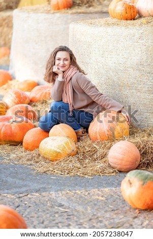 Young smiling woman sitting among pumpkins.