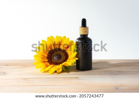 Black bottle for oil with a pipette. A jar with sunflowers on a wooden table. Mockup of cosmetics. Jar for cosmetic oil.