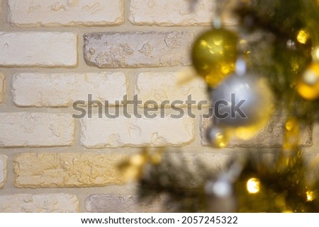 Decorative brick wall at the back of a Christmas tree with baubles, bows, animals, bells and glowing lights. Antique tiles in white, yellow and gray. Copy-space. Close-up with selective focus