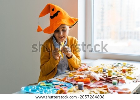 Caucasian girl in a witch costume sits at the table at home and prepares handicrafts for the Halloween holiday. Diy and decor in the room made of paper.