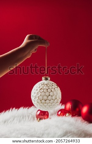 Children's hand holds a Christmas white ball decoration against of a white soft woolen blanket