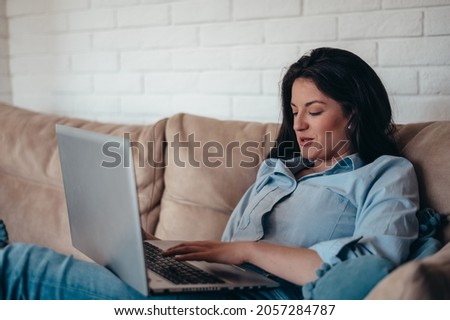 Beautiful young woman using laptop while sitting on the couch at home and relaxing