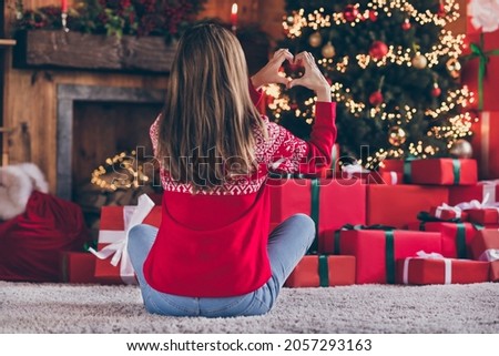 Photo of cute pretty young woman dressed red sweater showing hands arms heart celebrating new year smiling indoors room home house