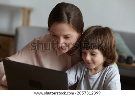 Mom and son using the laptop together, surfing the Internet, shopping, and playing games. Mother nanny babysiter helping the child pupil preschooler learning remotely online at the computer.