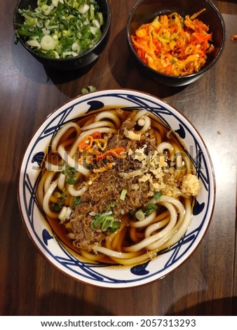Top view and selective focus of a bowl of Niku Beef Udon at a Udon Restaurant.  A typical Japanese udon noodle dish with kakedashi soup, fish stock soup and then topped with beef sukiyaki