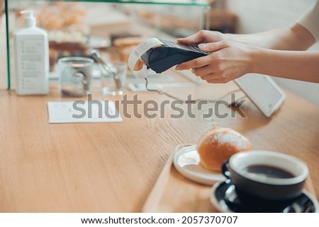 Female barista using terminal for contactless payment in cafeteria