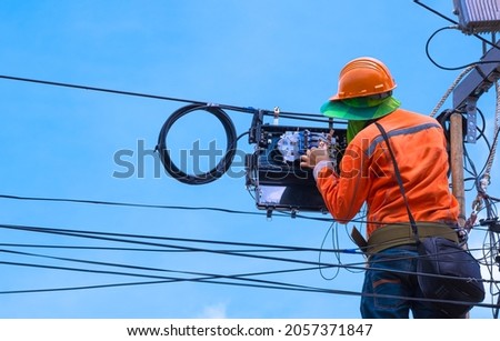 Technician on wooden ladder Checking Code numbers of Fiber Optic Cable lines in Internet Splitter box for Repairing to work normally on electric pole against blue sky background Royalty-Free Stock Photo #2057371847