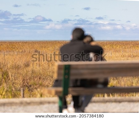 Back view of young couple blurred sitting on the bench and leaning their heads on each other. The man hugg his girlfriend. Autumn season. Street view, travel photo, blurred