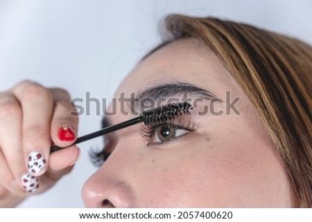 An asian woman styles her eyelashes with a lash roller. Closeup view.