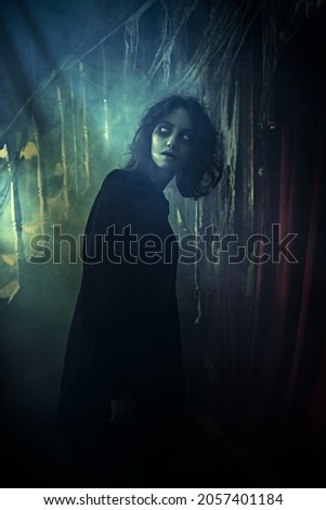 House ghost. A dreadful lonely ghost girl in black robe wanders through a dark abandoned house shrouded by haze and dust. Horror. Halloween.