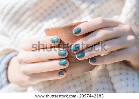 Female hands with blue nail design. Glitter blue nail polish manicure. Woman hands hold brown ceramic cup on white wool background