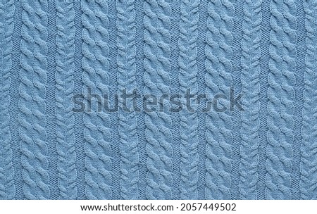 Texture of smooth knitted blue sweater with pattern. Top view, close-up. Handmade knitting wool or cotton fabric texture. Background of knitting patterns with a vertical Braid Cable.
