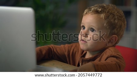Cinematic shot of curious toddler baby boy is watching movie or cartoon on laptop at home. Concept of technology, new generation, family, connection, vision of the future of children with web.