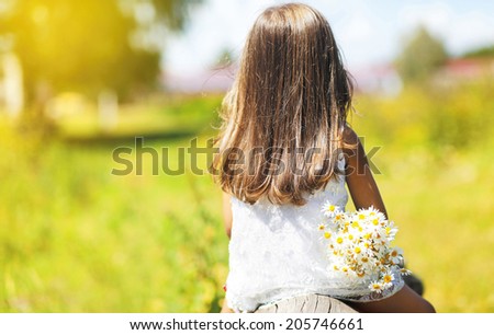 Rear view, silhouette little girl child sitting with flowers enjoying nature on summer blurred background in the park