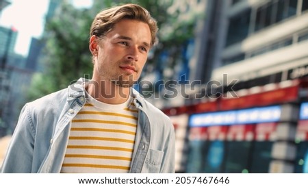 Portrait of a Happy Handsome Young Man in Casual Clothes Posing on the Street. Successful Male Model in Big City Living Urban Lifestyle. Background with Office Buildings and Billboards. Dutch Angle. Royalty-Free Stock Photo #2057467646