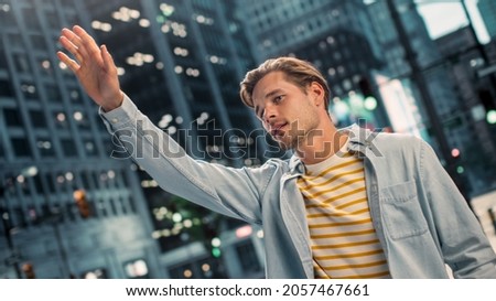 Portrait of a Happy Handsome Young Man in Casual Clothes Raising Hand to Catch a Taxi on the Street. Successful Male Model in Big City Living Urban Lifestyle. Shot with Dutch Angle. Royalty-Free Stock Photo #2057467661