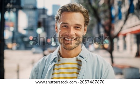 Portrait of a Happy Handsome Young Man in Casual Clothes Posing on the Street. Successful Male Model in Big City Living the Urban Lifestyle. Background with Office Buildings and Billboards. Royalty-Free Stock Photo #2057467670