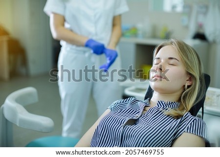 Patient, lying in the dental chair, waits for the dentist to come up to the chair and putting on gloves