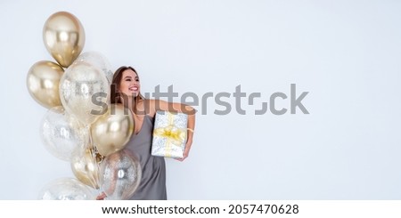 Photo of amazing laughing happy positive girl holds large wrapped giftbox and many air balloons. came to party. Celebration. New Year. Happy birthday. 8 March. Merry Christmas. Advertisement 