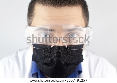 Close-up of a doctor wearing foggy goggles. The therapist in mask and eye protection looks directly into the frame with a tired gaze. Infection control concept and covid-19