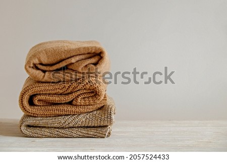 Bunch of knitted warm pastel color sweaters with different knitting patterns folded in stack, clearly visible texture. Stylish fall-winter season knitwear clothing. Close up, copy space for text.