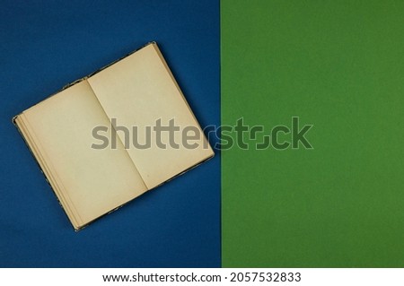 old open book with blank pages is lying on green and blue background. Copy space. Top view    