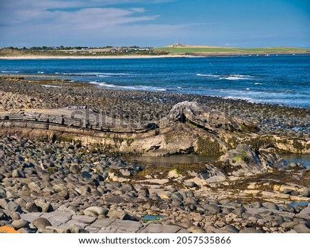 The folded rock strata of Greymare Rock on the Northumberland coast, near Dunstanburgh Castle. An outcrop of the Whin Sill, a tabular layer of the igneous rock dolerite in north east England, UK. Royalty-Free Stock Photo #2057535866