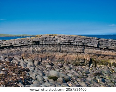 The folded rock strata of Greymare Rock on the Northumberland coast, near Dunstanburgh Castle. An outcrop of the Whin Sill, a tabular layer of the igneous rock dolerite in north east England, UK. Royalty-Free Stock Photo #2057536400