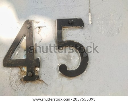 Black metal number 45 house number on white wall background. Forty five digit. close up
