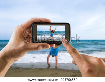 man taking a picture with your mobile phone a one man doing cartwheel on sand  on the beach
