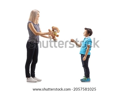 Full length profile shot of a woman giving a teddy bear to a boy isolated on white background