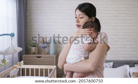 asian first time mom is holding her cute little baby upright by supporting its neck with her hand in the bedroom with white wall at background. Royalty-Free Stock Photo #2057600750