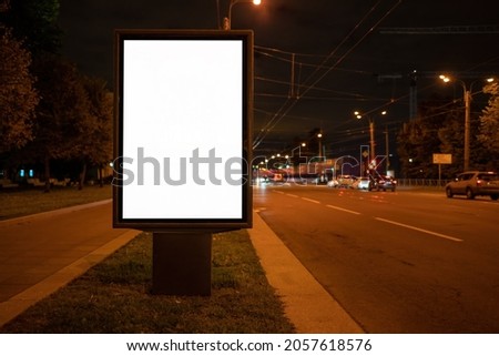 Billboard at night near the road. Glowing vertical poster.